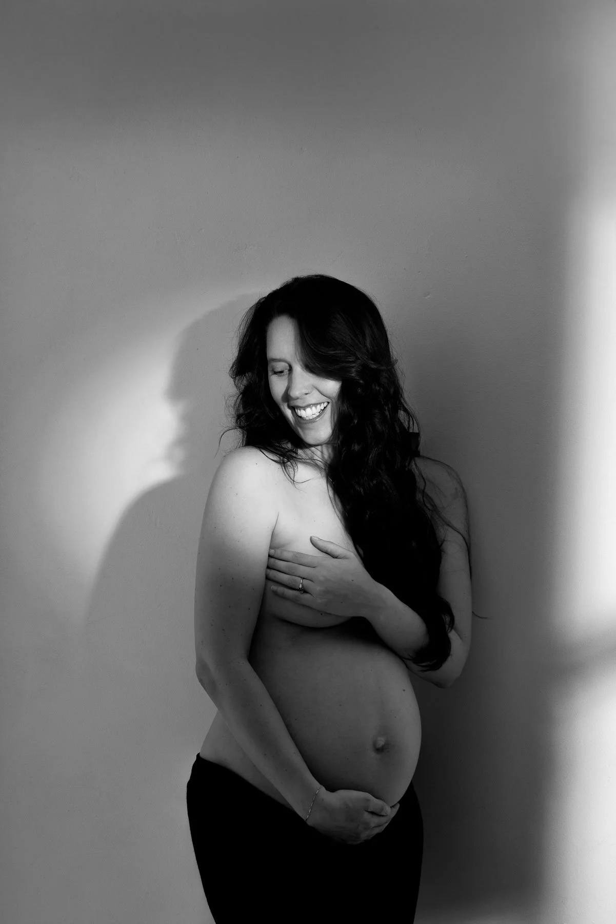 Pregnant woman holding her breasts, wearing black skirt, shadows