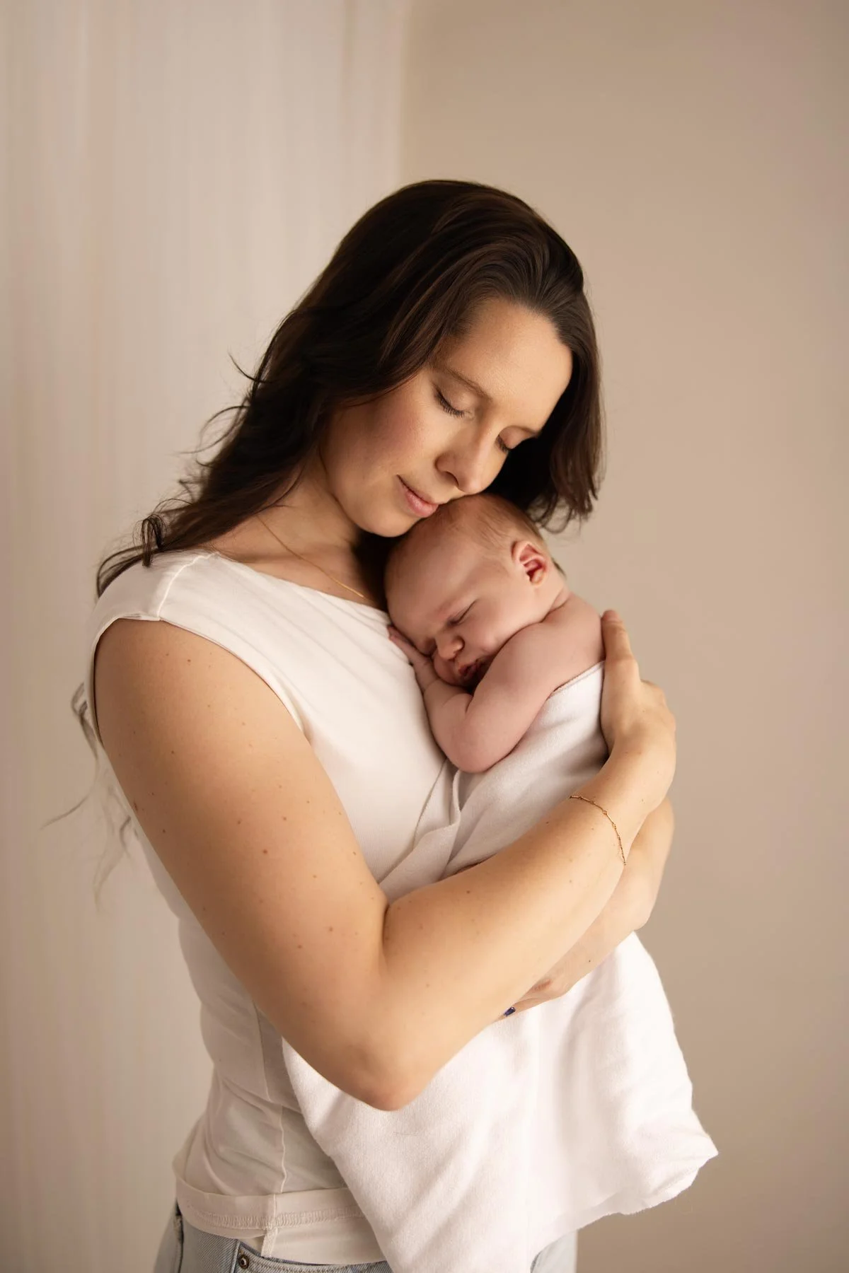 Mother holding a sleeping baby wrapped in a white blanket.