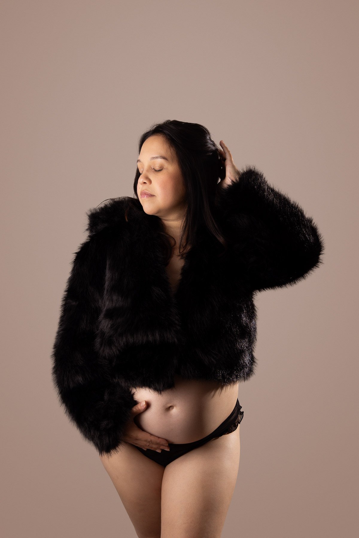 Asian dark short hair pregnant beautiful woman wearing a crop fur coat and touching her belly.