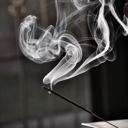Rauch von einem brennenden Räucherstäbchen, der sich in der Luft kräuselt.
