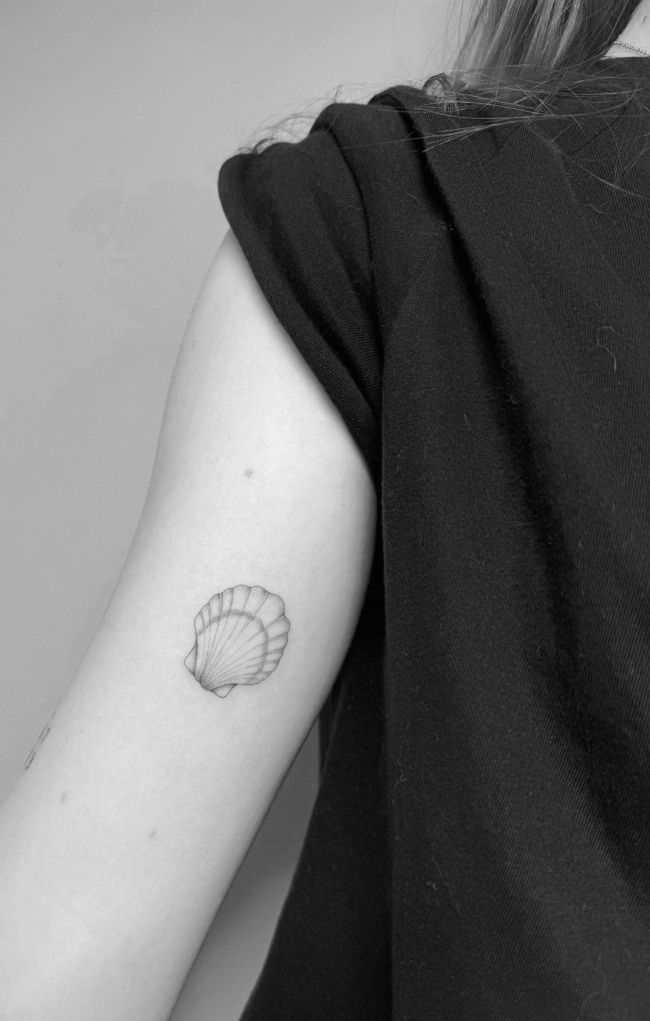 Schwarzweiß-Bild von einem Arm mit einem Muscheltattoo auf der Oberseite.