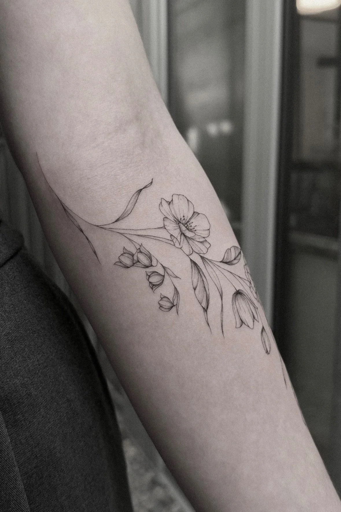 Blumentattoo am Arm, zeigt filigrane Blumen und Blätter in Schwarz-Weiß.
