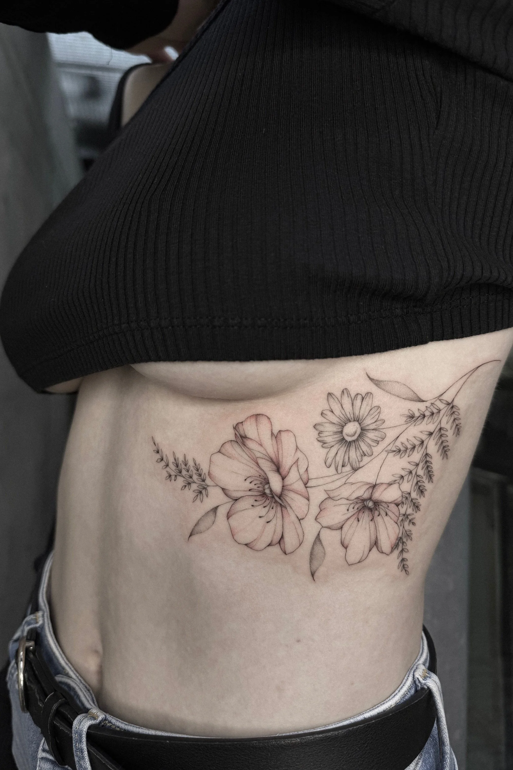 Blumentattoo an der Seite eines Körpers, das Details von Blumen und Blättern zeigt.