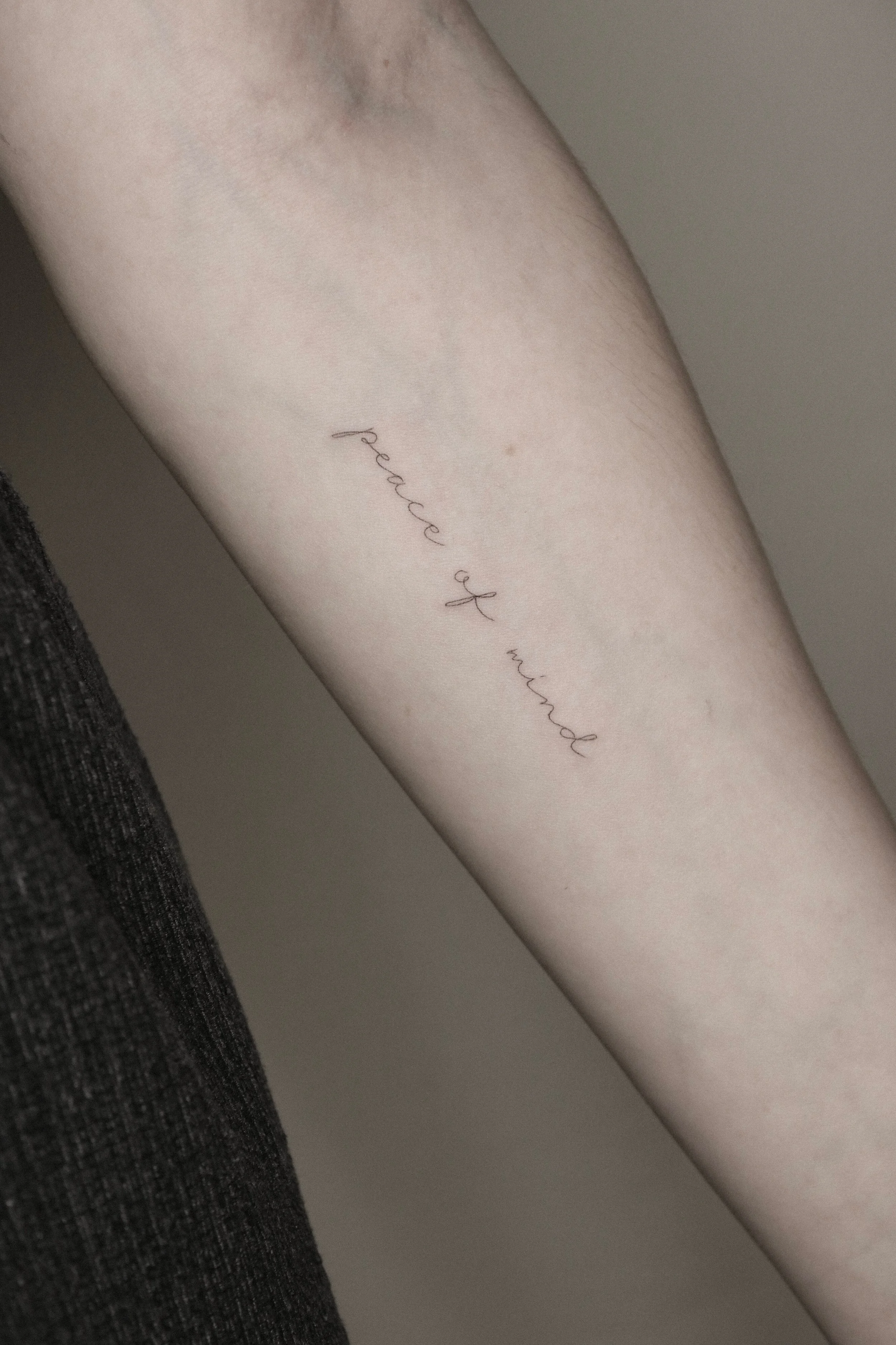 Arm mit einem Tattoo, das den Text "peace of mind" zeigt.