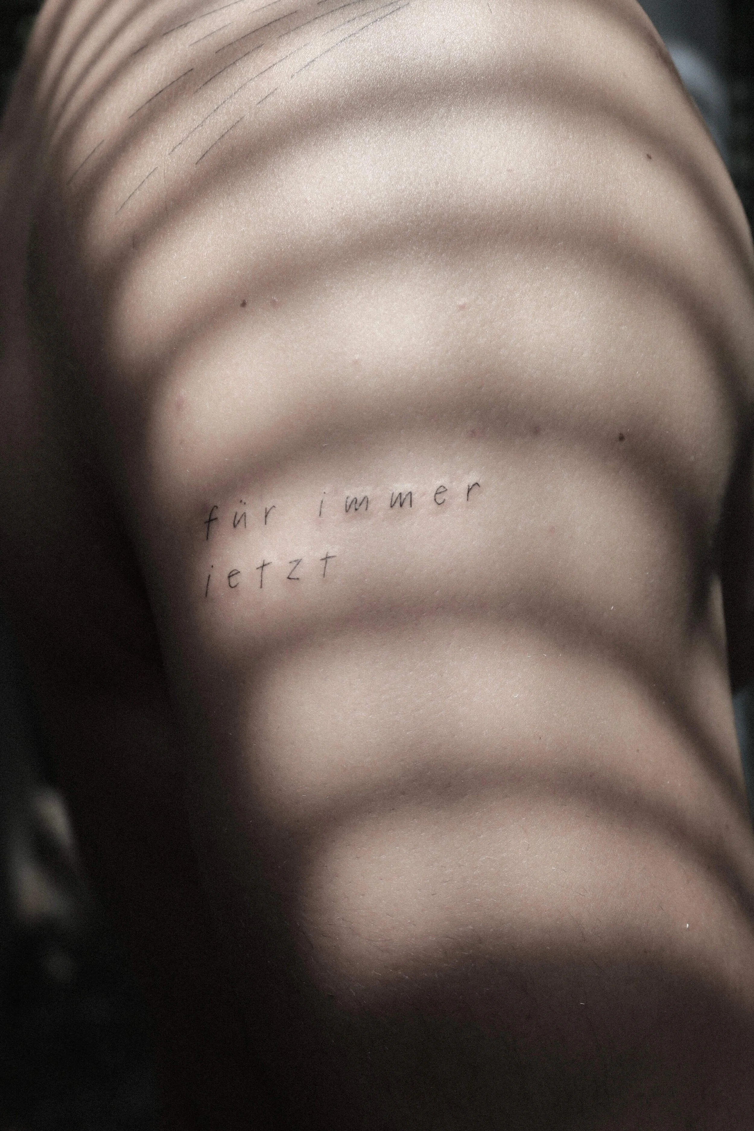 Rückenszene mit einem Tattoo mit dem Text "für immer jetzt" und Schattenstreifen.