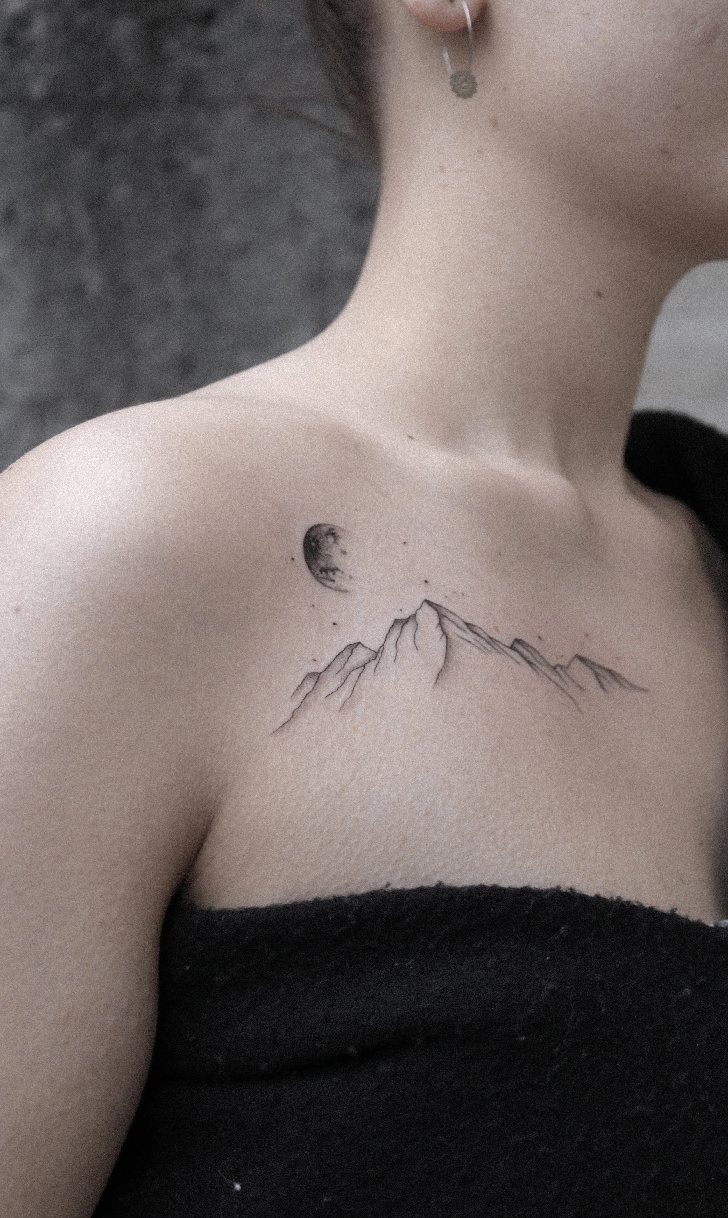 Nahaufnahme einer Person mit einem Tätowierungsmotiv auf der Schulter, das Berge und den Mond zeigt.