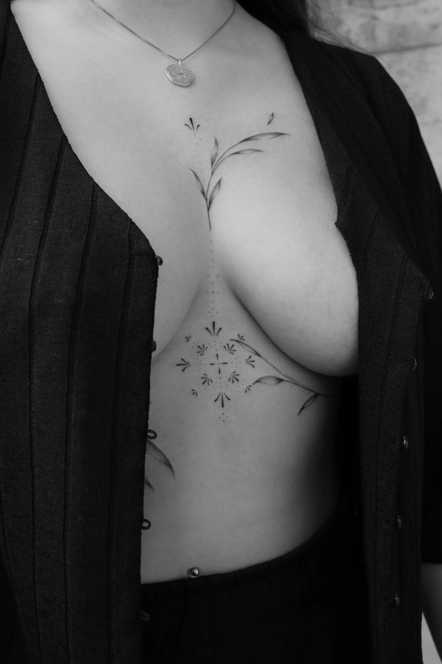 Nahaufnahme eines Brust- und Dekolletébereichs mit floralem Tattoo und Schmuck an der Halskette.