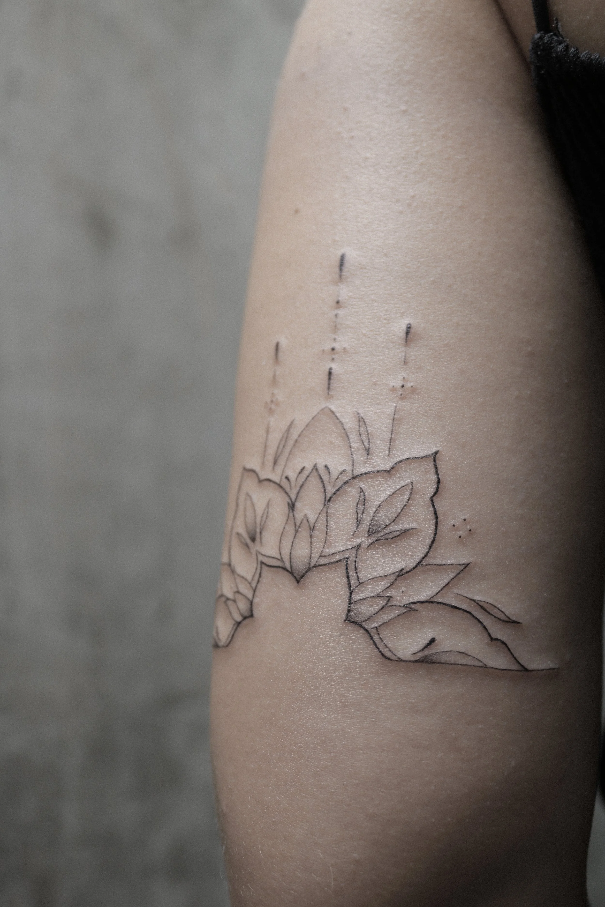 Minimalistisches florales Tattoo auf einem Oberarm, das aus feinen Linien besteht.