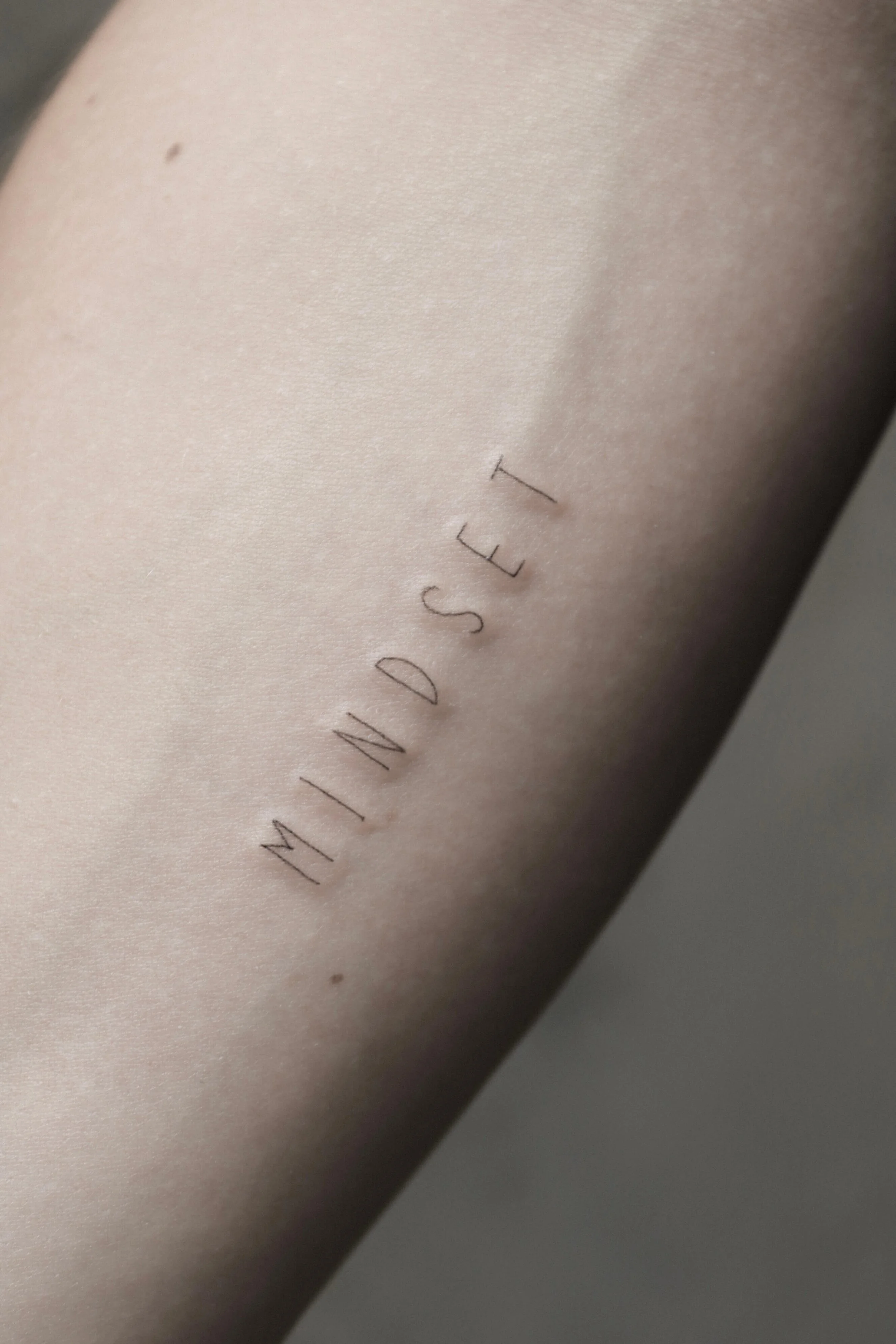 Arm mit Tätowierung des Wortes "MINDSET" in feiner Schrift.