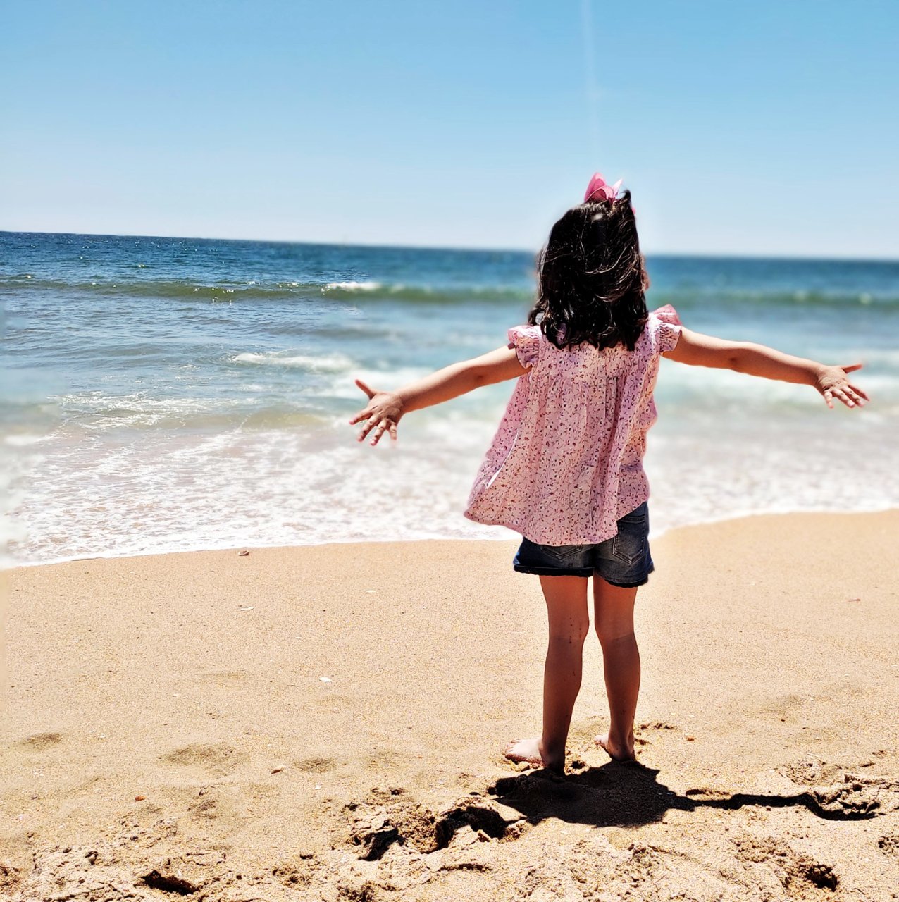 A girl on a beach wearing a woven top and shorts.