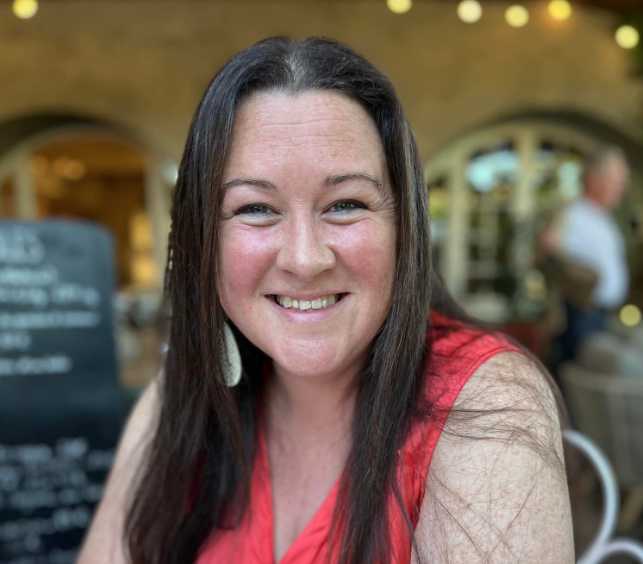 Woman with long brown hair smiling in a restaurant or cafe setting.