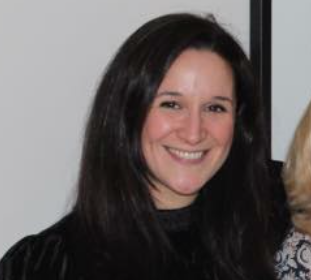 A woman with shoulder-length dark hair smiling at the camera, in an indoor setting.