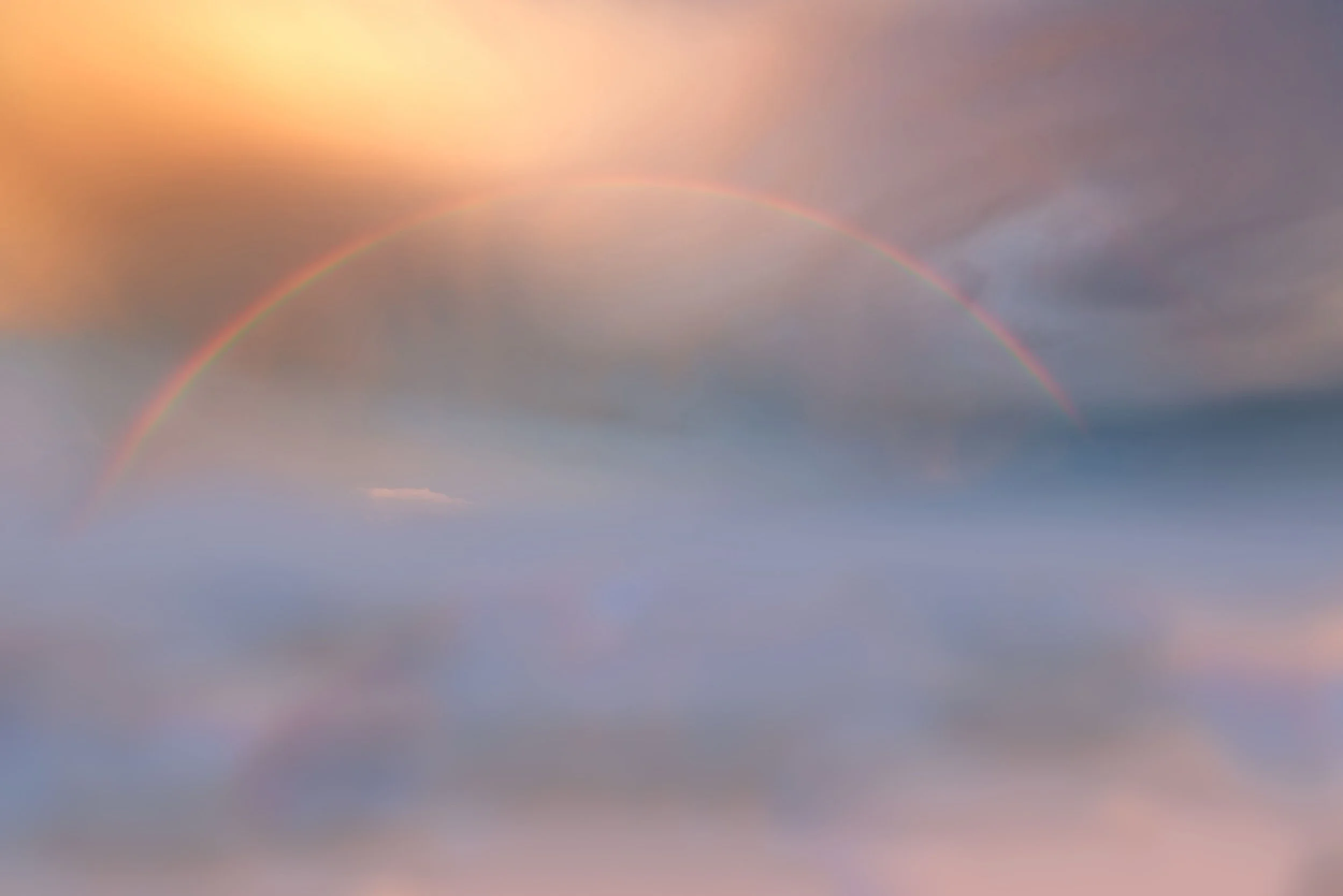 A rainbow arching across a cloudy sky with soft pastel hues.