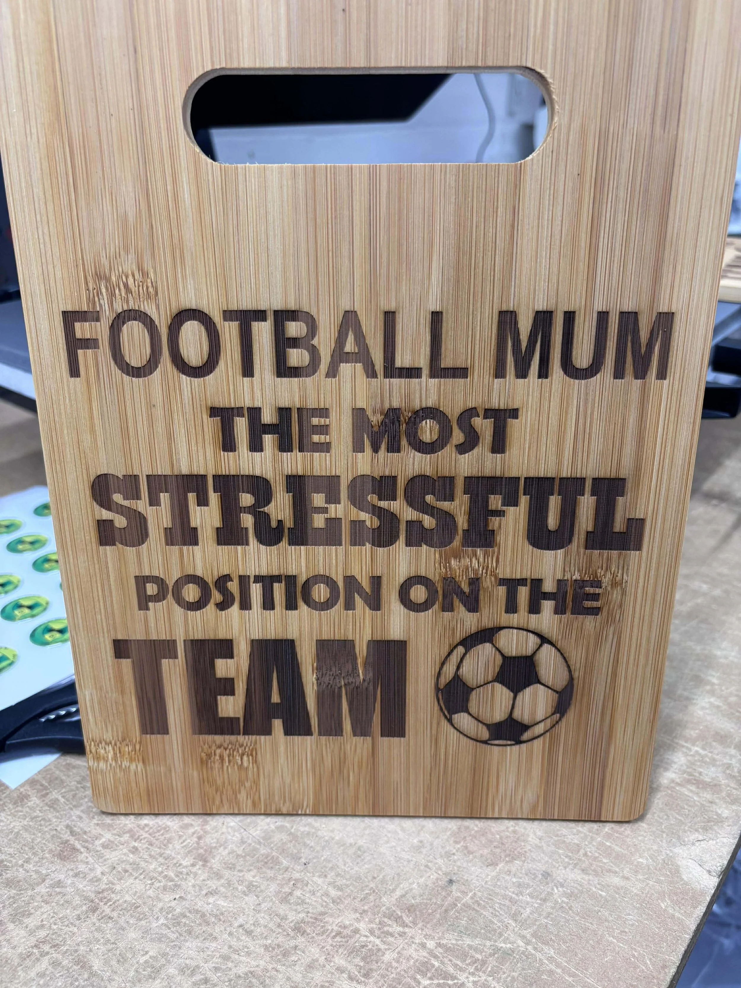 Wooden plaque with engraved text that reads 'Football Mum The Most Stressful Position on the Team' alongside a soccer ball graphic.