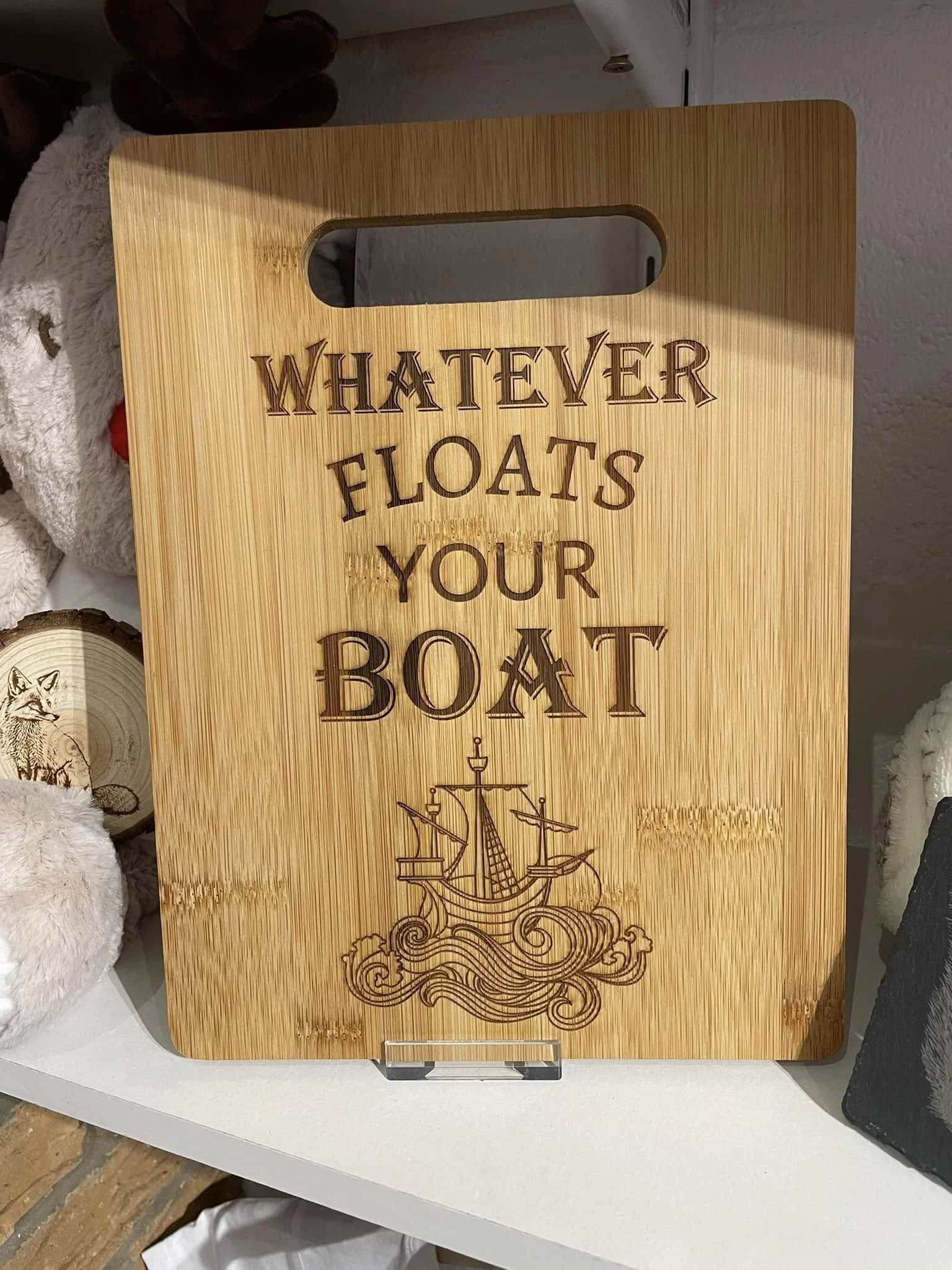 Wooden sign with cut-out handle that reads 'Whatever floats your boat' and features a drawing of a sailing ship on ocean waves.