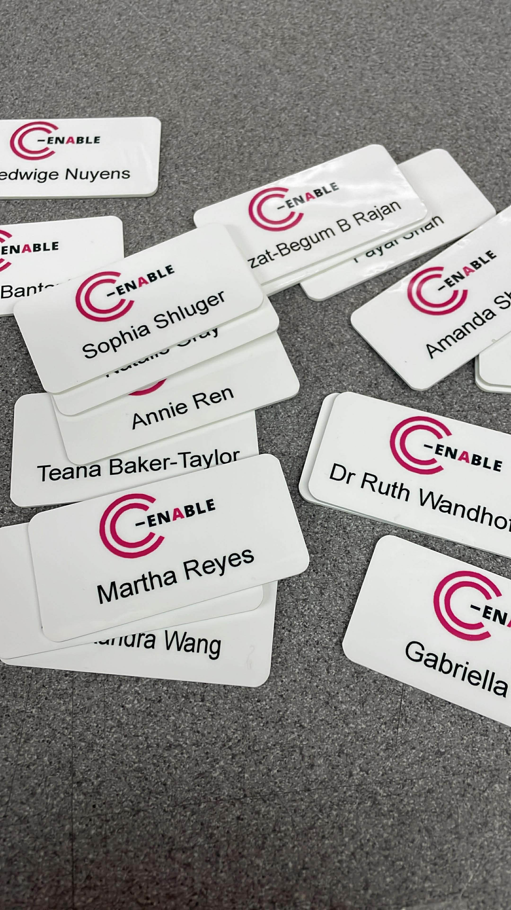 Name tags with the logo 'C-ENABLE' scattered on a gray surface.