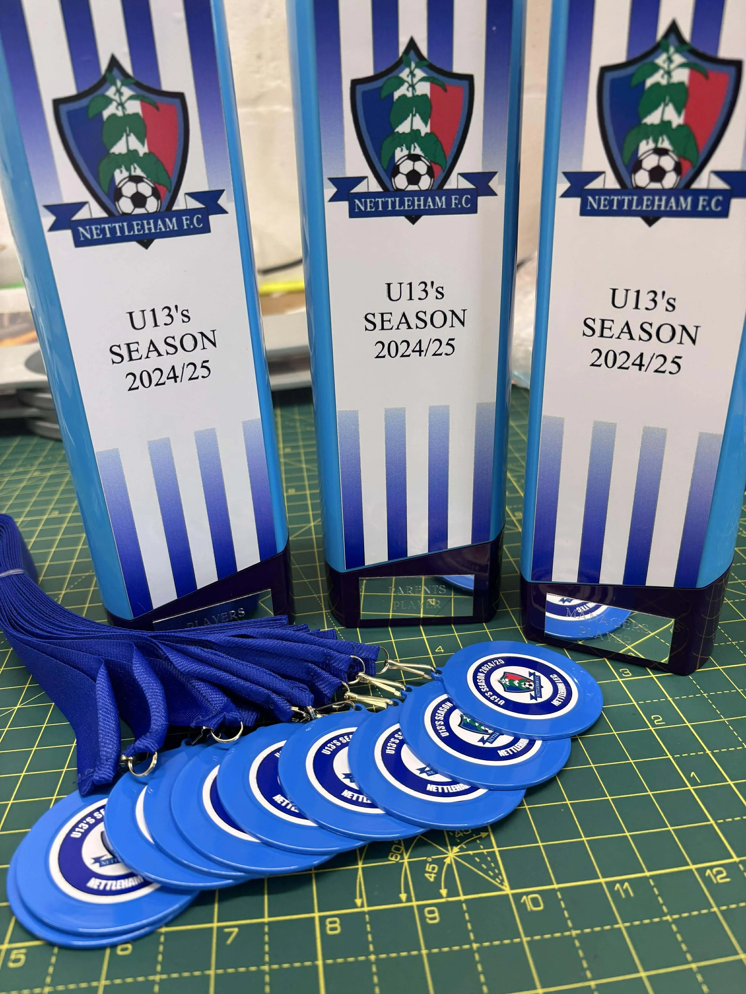 Nettlerham F.C. U13's season 2024/25 medals and awards on a green cutting mat.