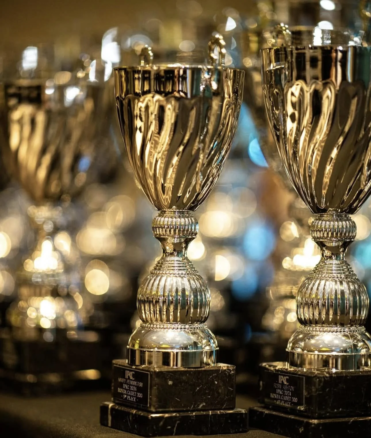 Silver trophies with black bases, displayed on a table at an award ceremony.