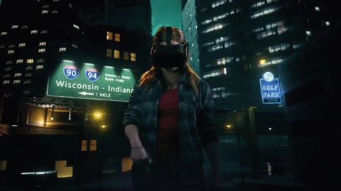 A person wearing a virtual reality headset in a cityscape at night with highway signs for I-90 and I-94 towards Wisconsin and Indiana.