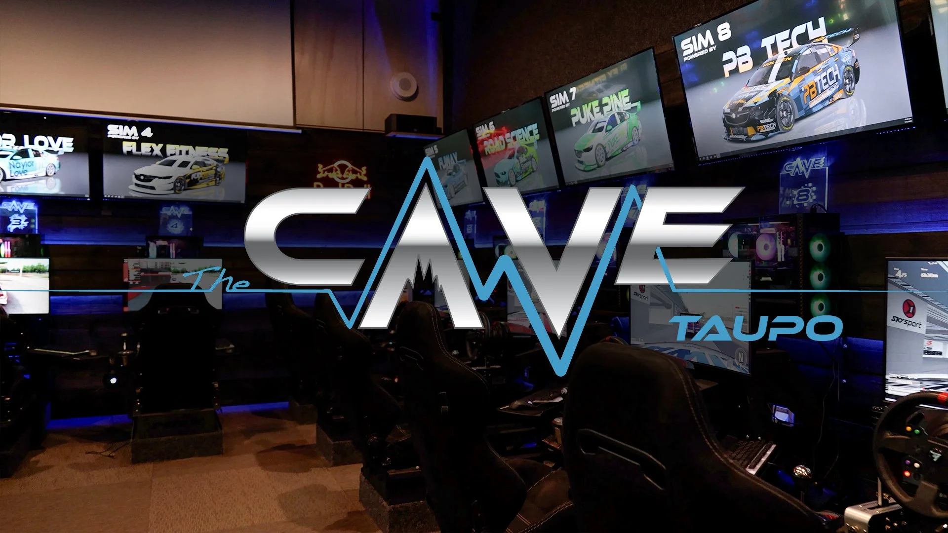 Racing simulator setup at The Cave Taupo with multiple screens displaying car simulation graphics. Several racing seats and steering wheels are visible.