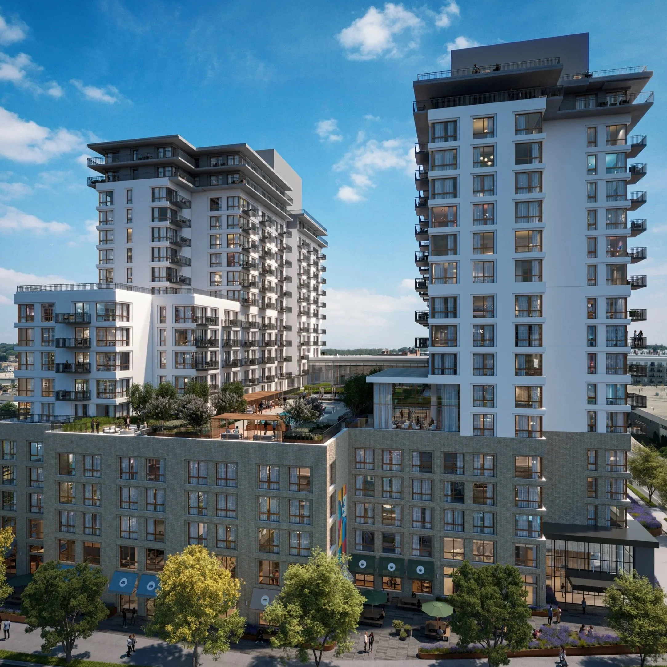 Modern multi-story residential buildings with glass windows and balconies, surrounded by trees and a public space with people walking and sitting.