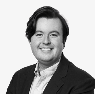 Black and white photo of a smiling man with dark, wavy hair wearing a suit jacket and collared shirt.