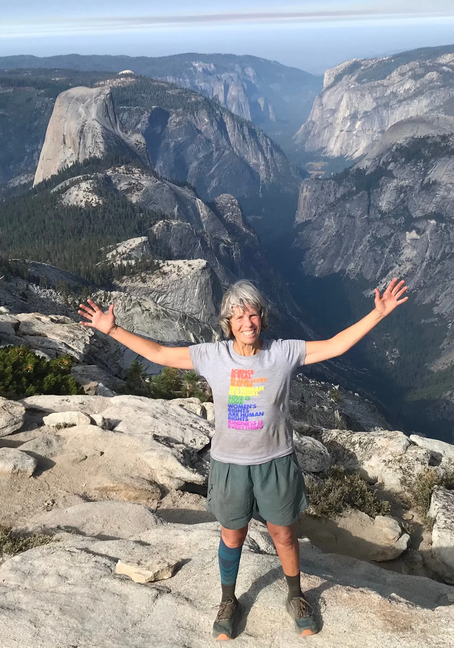 Kathy on top of mountain with arms outstretched