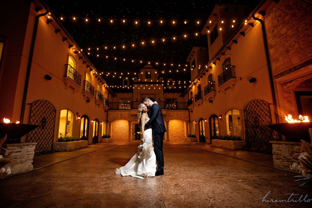 A bride and groom in an outdoor area embracing at night under hanging lights