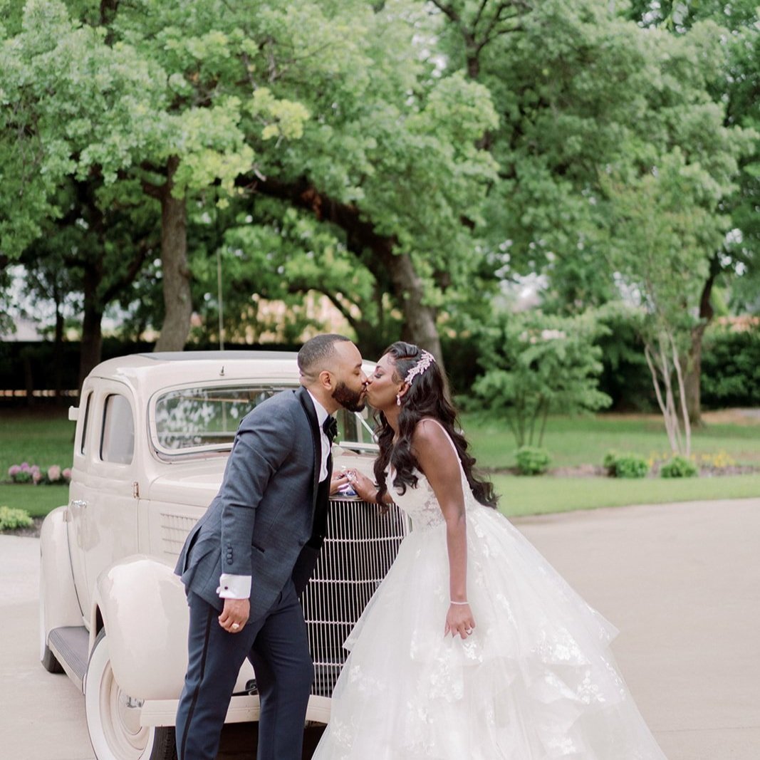 a bride and groom kiss while standing behind a vintage getaway car