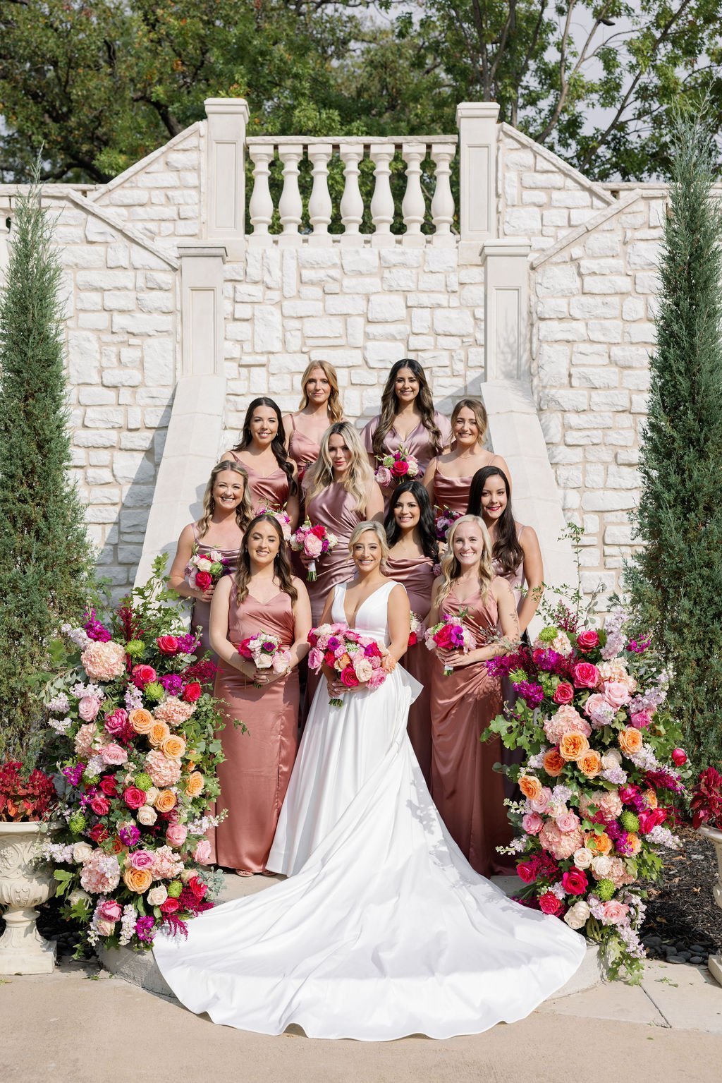a bride stands with her bridal party on a grand outdoor staircase in front of Brighton Abbey wedding venue