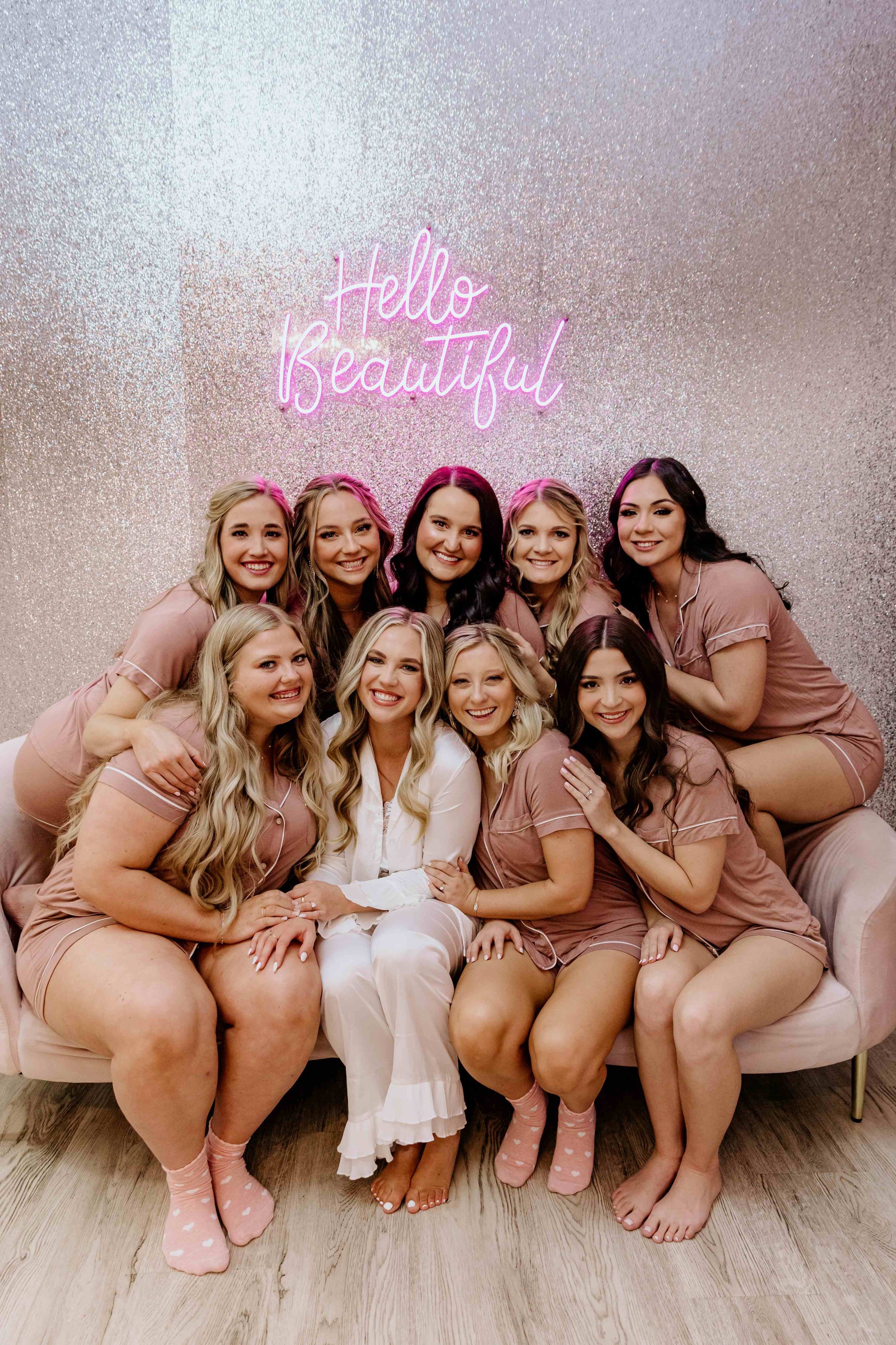 A bride poses with her bridal party inside a getting ready suite. They sit on a couch