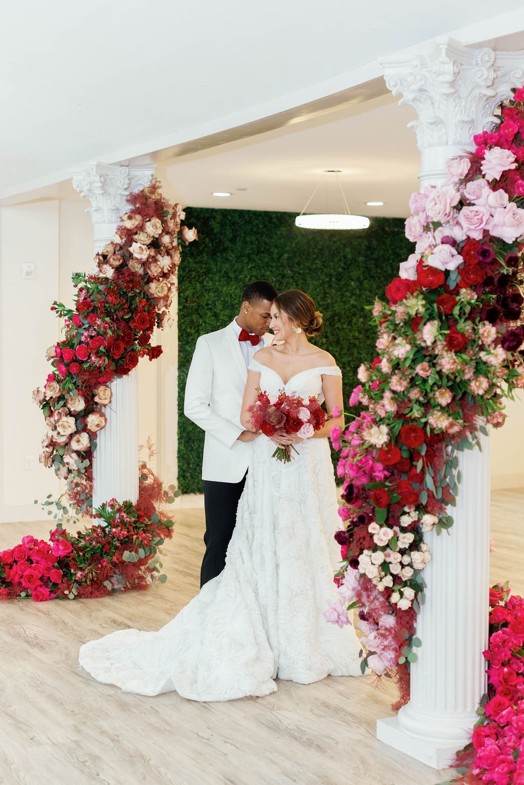 A bride and groom pose for formal photos in front of stunning flower arrangements wrapping around columns
