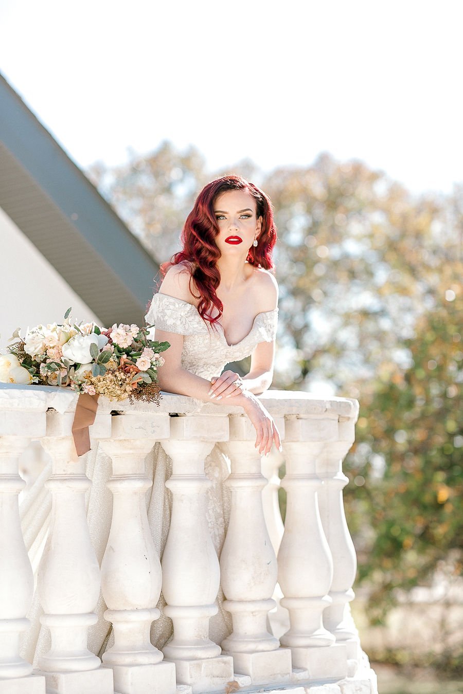 a bride in a stunning off the shoulder gown leans over a balcony surrounded by flowers