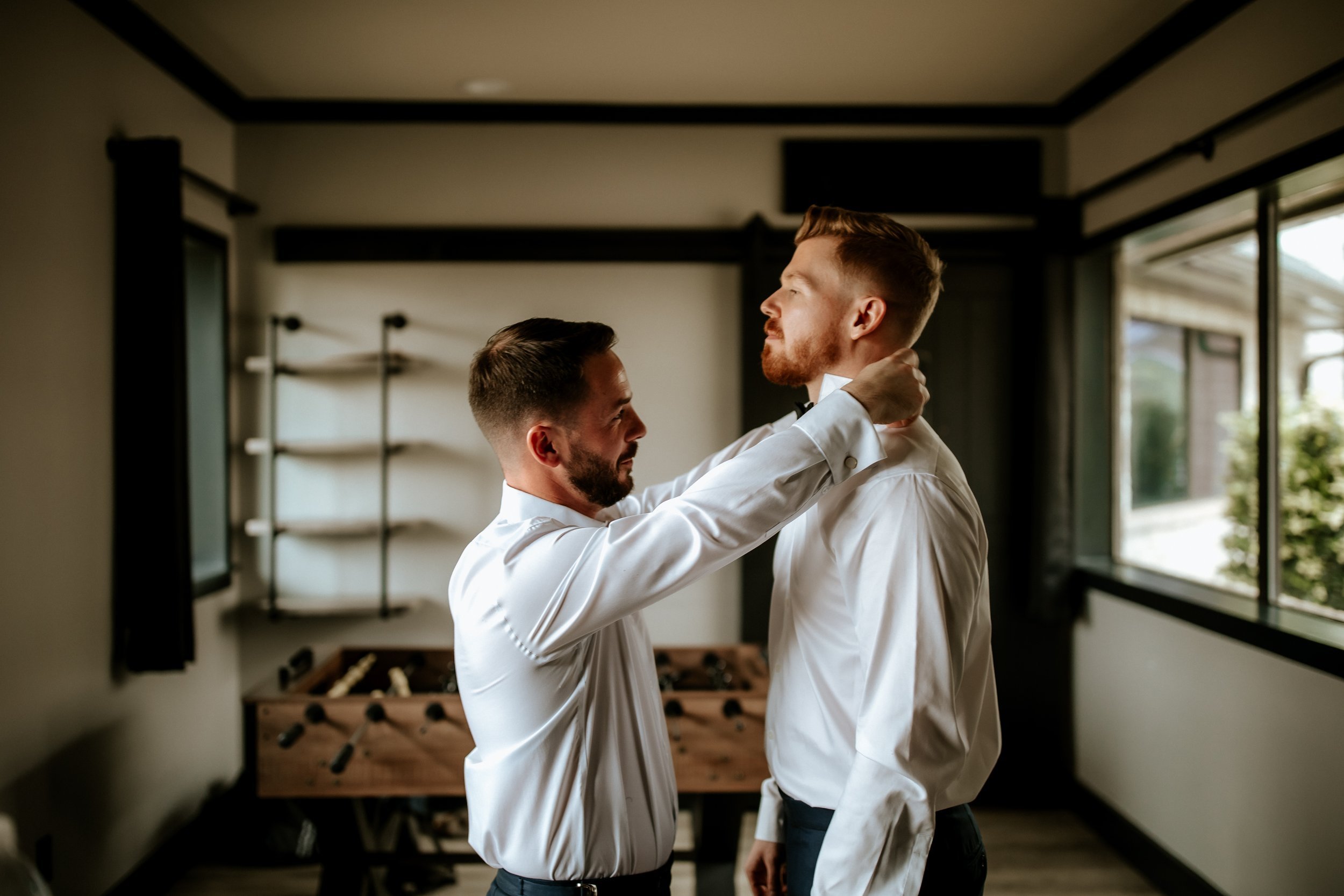 a groomsman helps the groom with his bow tie