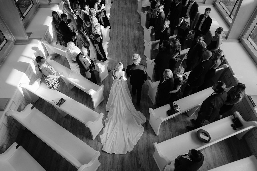 A view of a bride and her father walking down the aisle, from above, in black and white