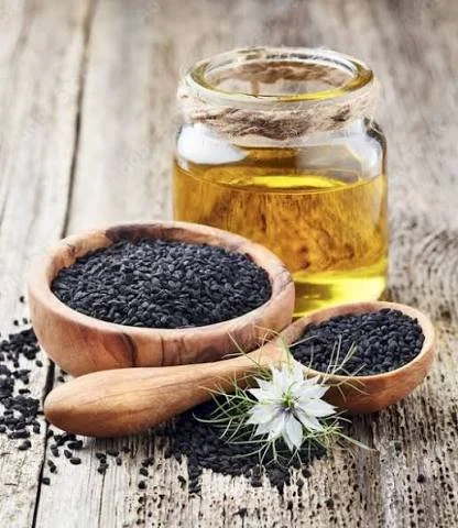 Black cumin seeds in a wooden ball with cumin seed oil in a jar behind it.