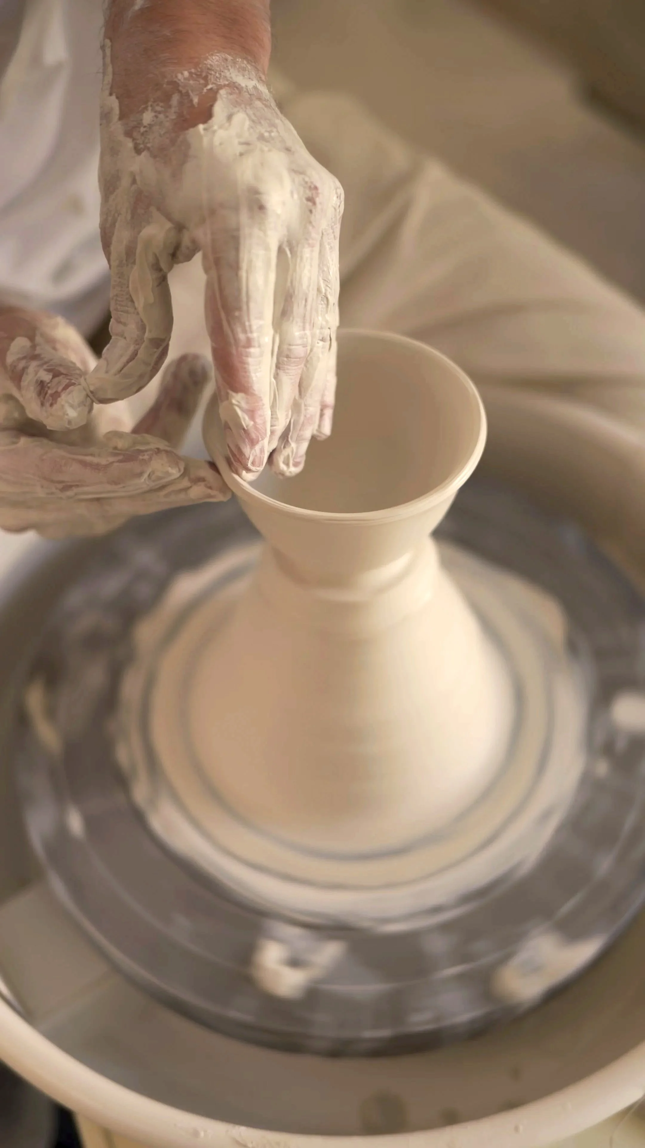 Hand eines Töpfers, der einen Keramiktopf auf einer Drehscheibe formt.