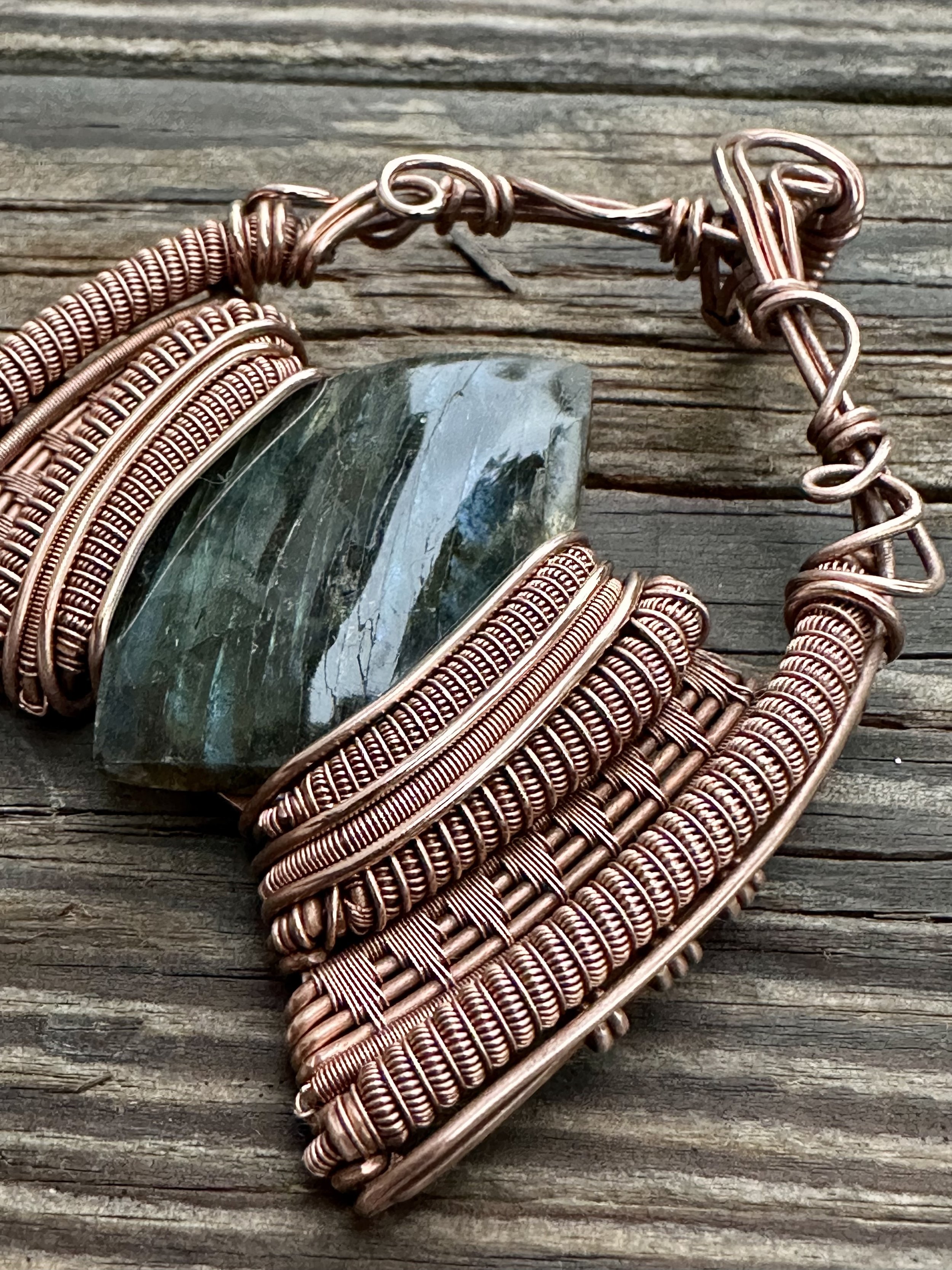 close-up view of iridescent labradorite stone intricately wrapped in copper wire showcasing the pendants detailed craftsmanship
