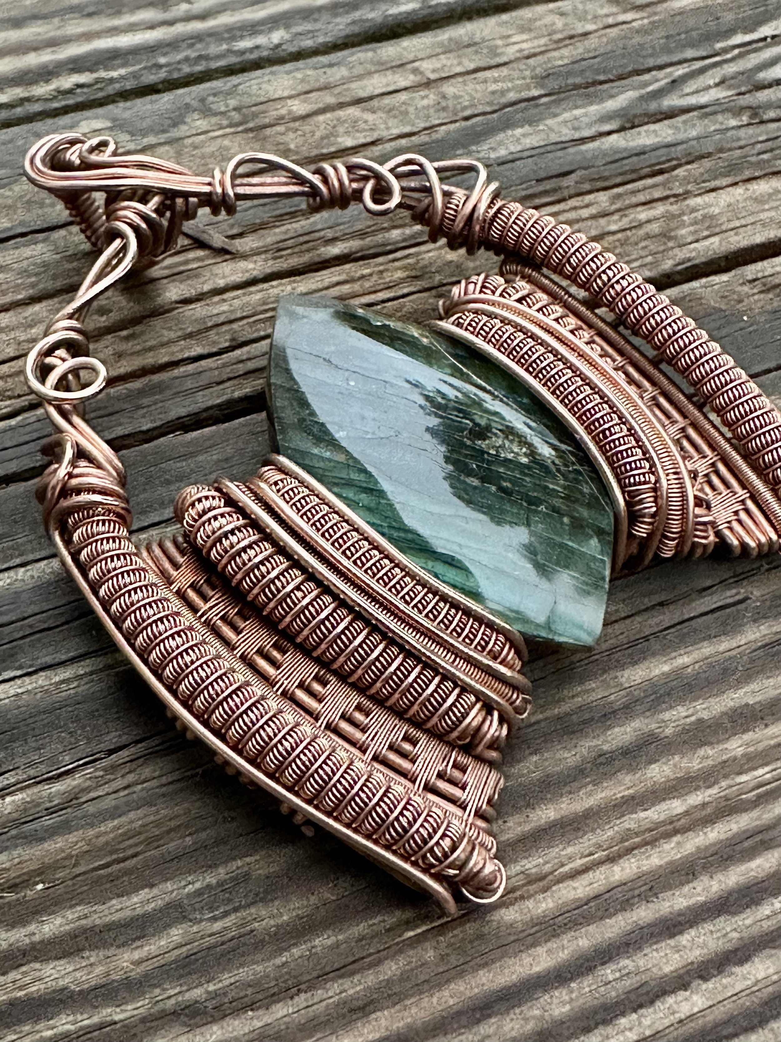 close-up view of iridescent labradorite stone intricately wrapped in copper wire showcasing the pendants detailed craftsmanship