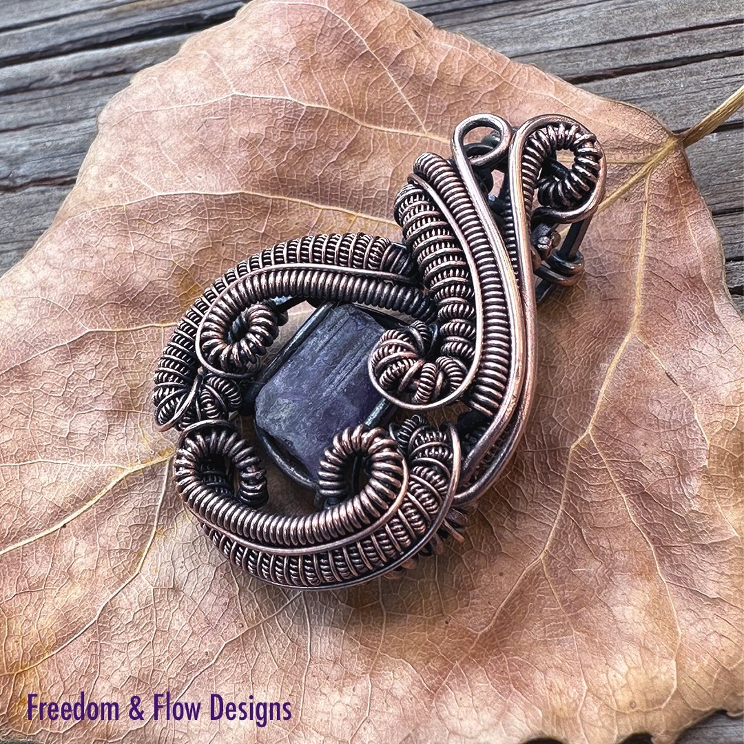 close-up of a handcrafted pendant featuring a radiant purple apatite gemstone set in intricately twisted copper