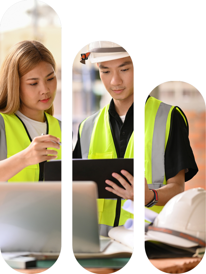 Two construction workers, a woman and a man, wearing high-visibility vests and hard hats, reviewing plans and using a laptop.