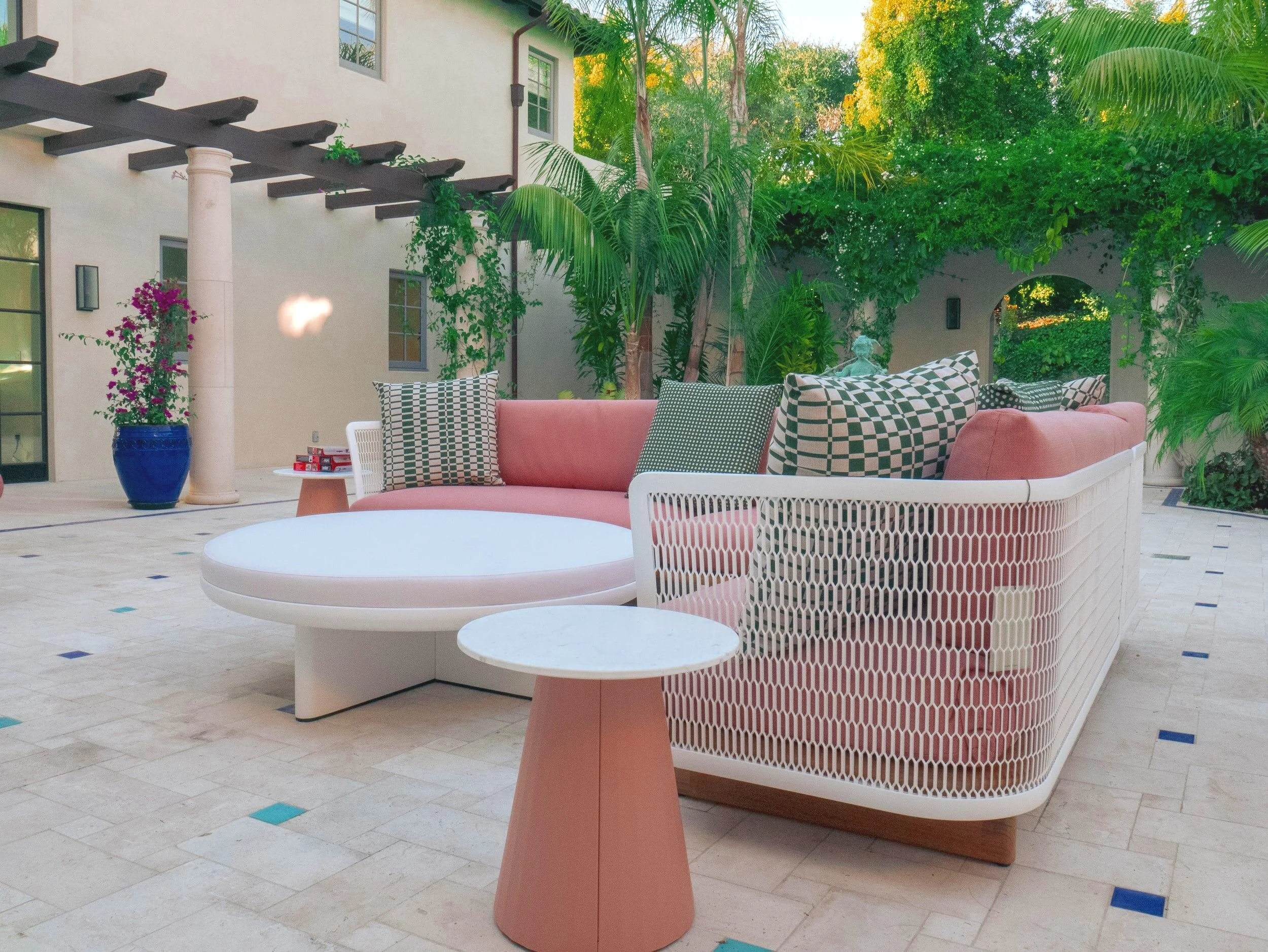 Outdoor patio with modern pink sofa, round white coffee table, small side table, and potted plants.