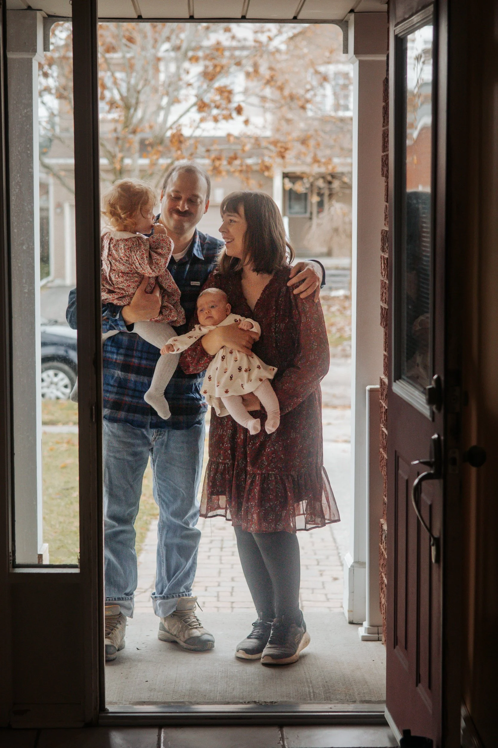 Family photography in uxbridge family of four through the doorway captured at a lifestyle newborn session in Uxbridge ontario "coming home" photo
