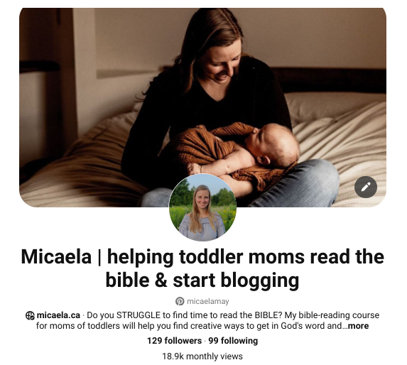 A woman sitting on a bed holding a sleeping toddler while smiling.