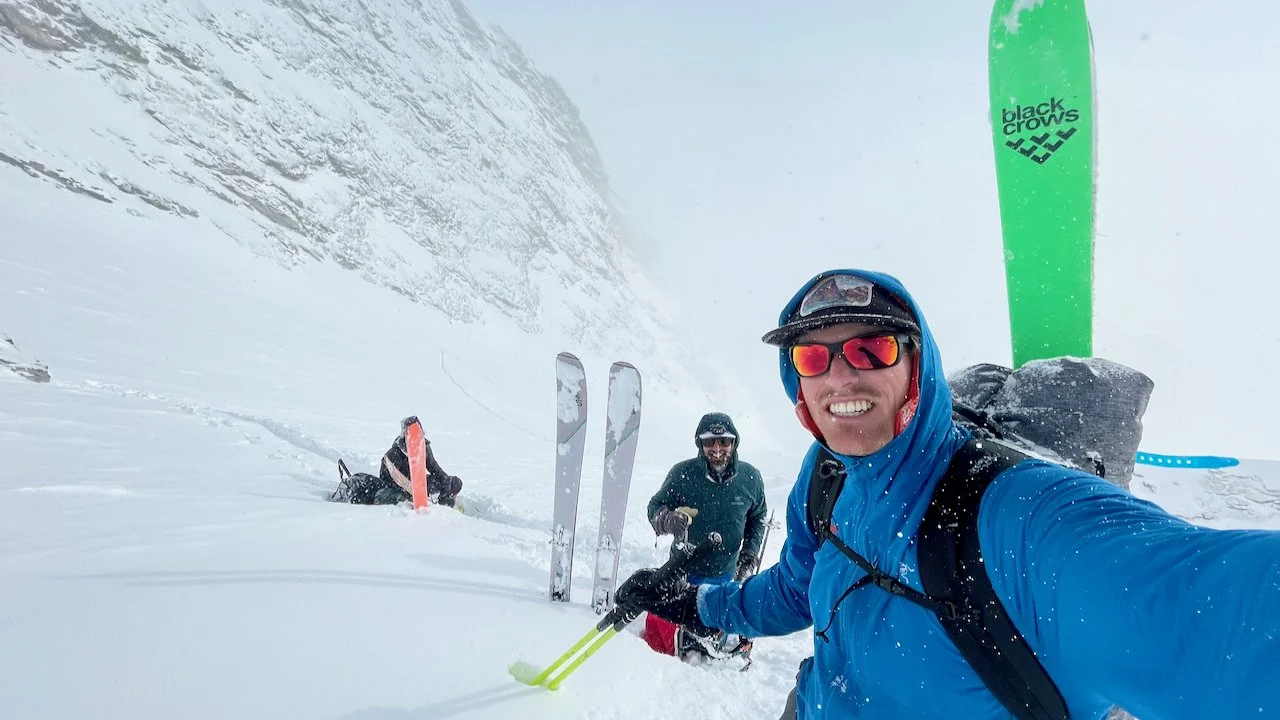 Three skiers take a break while climbing a steep snow slope in a storm.