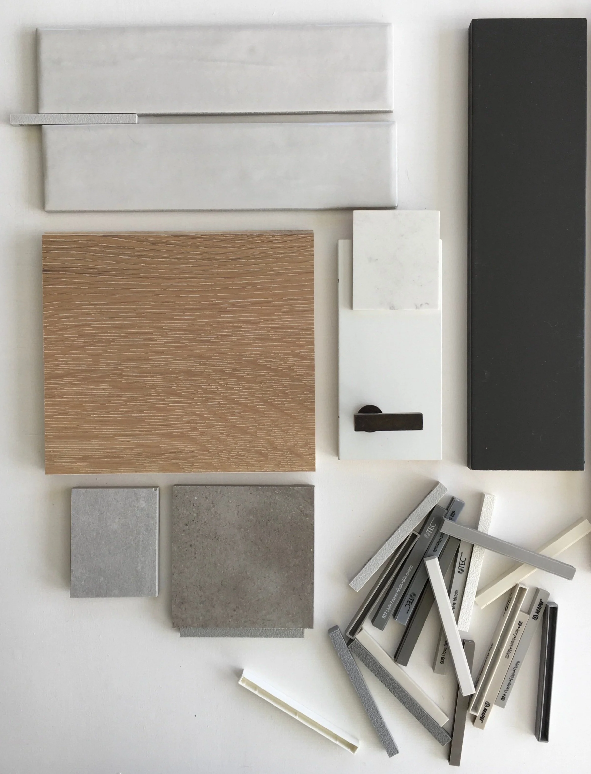 Collection of various material samples including wood grain, gray and white tiles, and metal strips on a white background.