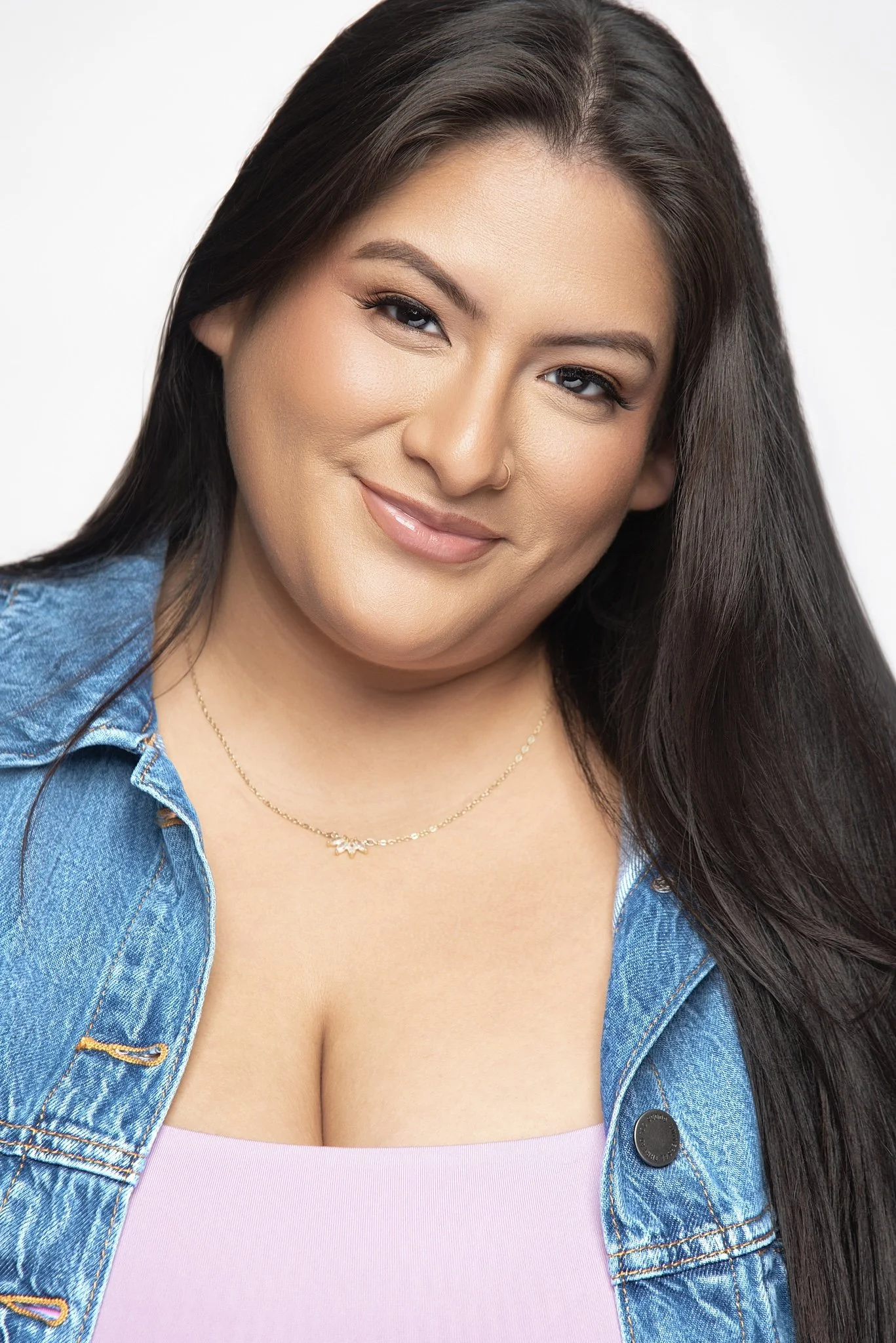 A woman with long dark hair, wearing a denim jacket over a pink top, smiling at the camera against a white background. Darius Nichols Photography DNPhotographyNYC