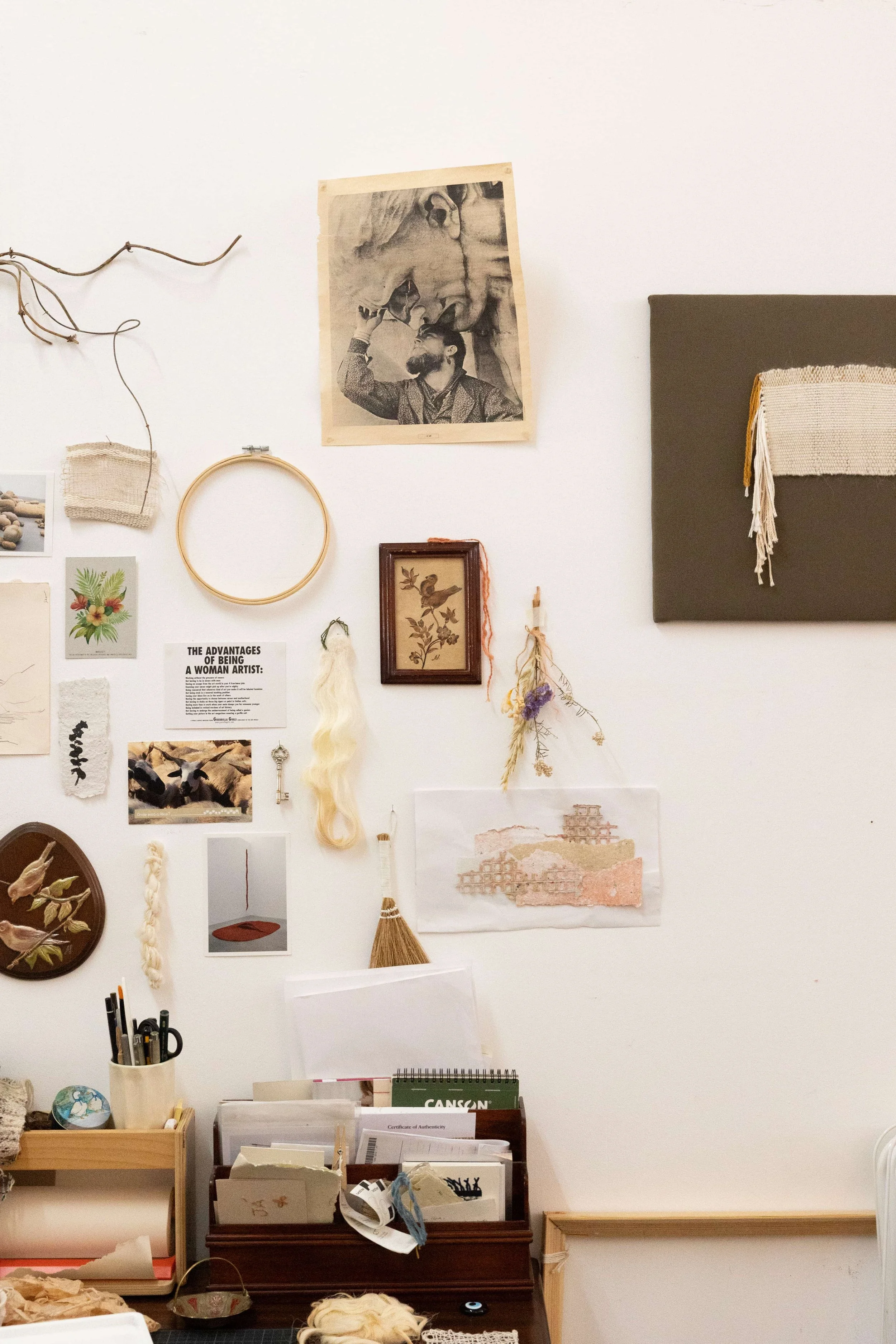 A wall decorated with various artwork, photographs, and decorative items. Mostly natural objects and weaving inspiration.