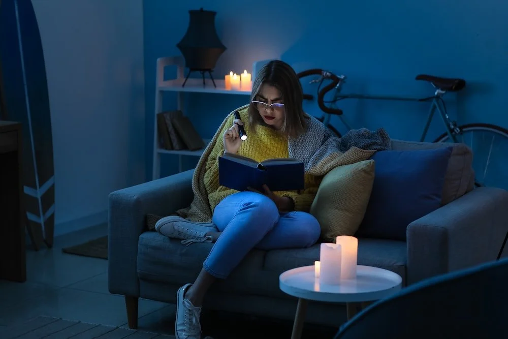 Wopman sitting on a couch in the dark reading by flashlight