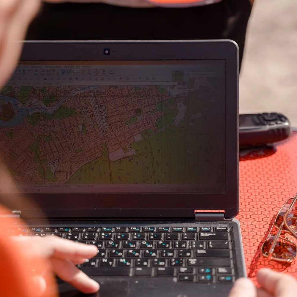 A person using a small laptop with a map displayed on the screen, sitting at a table with sunglasses and a smartphone nearby.